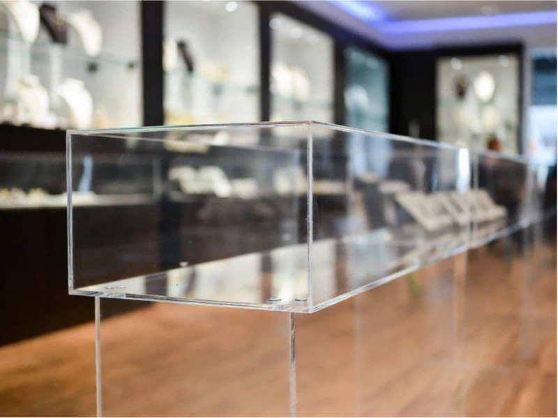 Premium clear acrylic display case in a high-traffic retail jewelry store environment requiring specific cleaning protocols to prevent chemical stress and cloudiness